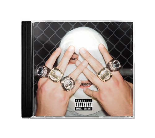 A person wearing a white face covering poses behind a "Heel Turn" CD with a Parental Advisory label, showing off bold rings on both hands. A chain-link fence in the background adds an edgy, post-punk touch to the scene.